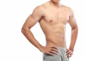 Shirtless man with a flat chest standing with his hands on his hips, representing male breast reduction for gynecomastia.