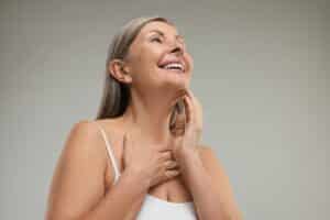 Smiling woman in her 50s shows off her smooth neck following neck liposuction and neck lift.