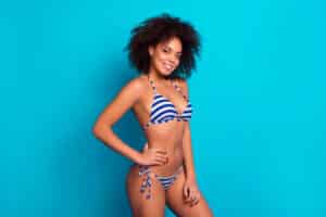 Biracial woman in striped swimsuit has elevated breasts after cosmetic lift.