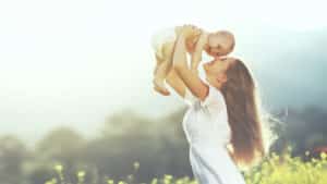 Young mother lifts her baby in celebration while visiting a field.